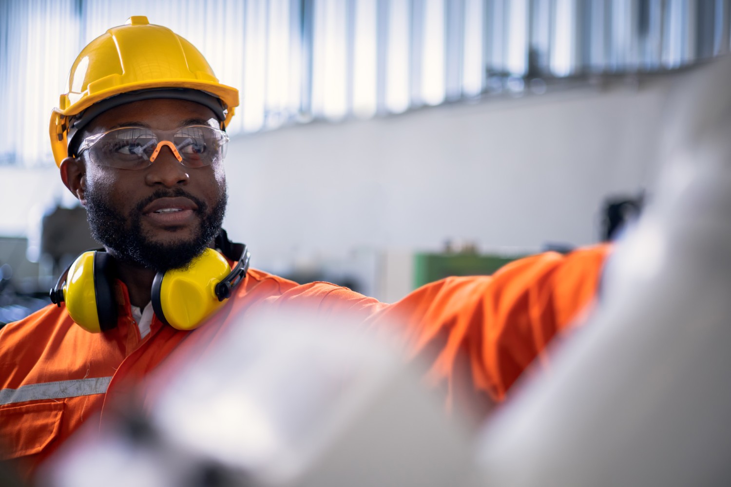 African engineer pointing to a robotic arm in factory.